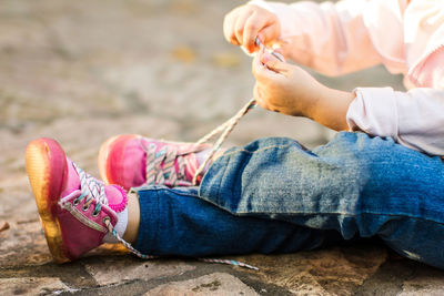 Low section of girl tying shoelace while sitting on footpath