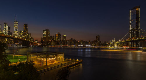 Illuminated buildings by river against sky in city at night