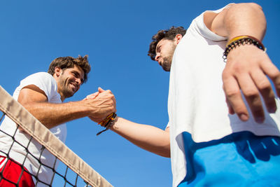 Low angle view of smiling tennis player holding hands at court