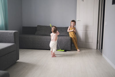 Baby 1 year old and older sister 3 years old with mop help mom clean living room with sofas