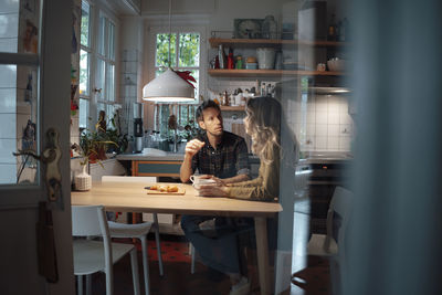 Man talking with girlfriend sitting at dining table in kitchen