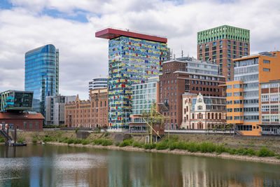 Buildings by river against sky in city