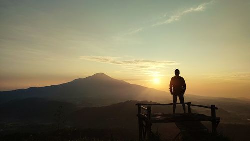 Rear view of man standing on mountain against sky during sunset