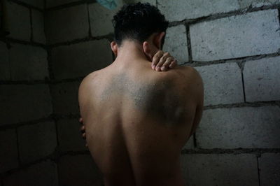 Rear view of shirtless man standing against brick wall