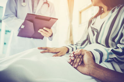 Midsection of woman holding hands on bed