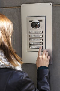 Rear view of woman using intercom on wall