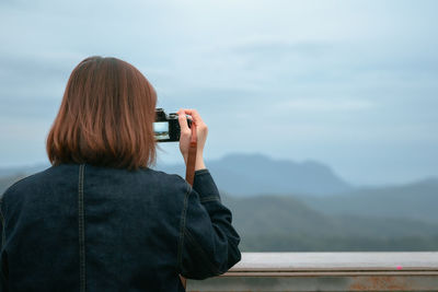 Rear view of woman photographing on mountain against sky