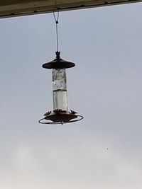 Low angle view of electric lamp hanging by building against sky