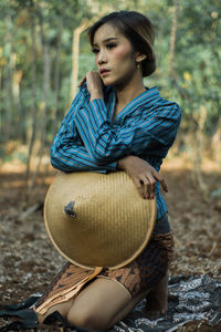 Young woman wearing hat while sitting on land