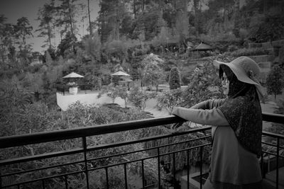 Woman standing by railing against trees