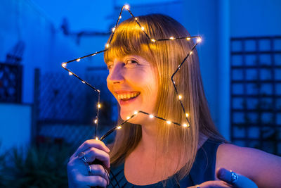 Close-up portrait of smiling woman holding illuminated star shape