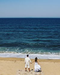 Rear view of couple on beach against clear sky