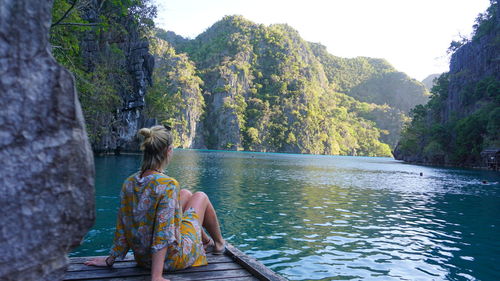 Rear view of woman sitting by lake against trees