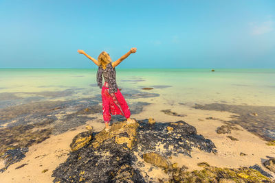 Woman with arms outstretched standing at beach against sky