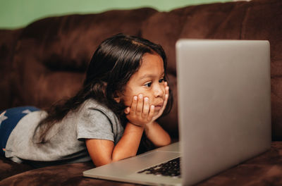 Cute girl using laptop while lying on sofa at home