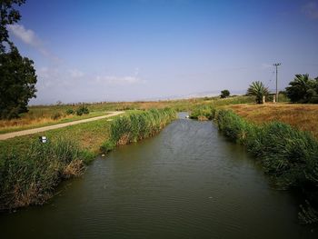 Scenic view of canal amidst field against sky