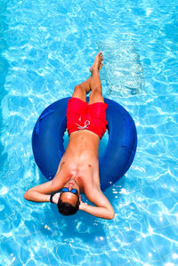 High angle view of shirtless man lying on inflatable ring in swimming pool