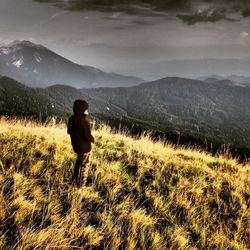 Rear view of child standing on field against mountains