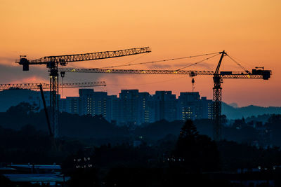 Cranes against buildings during sunset