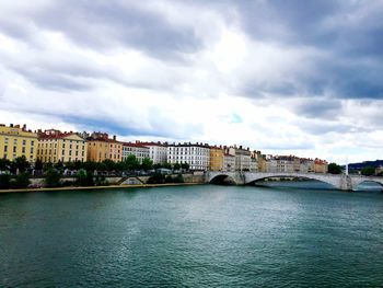 Bridge over river by buildings in city against sky