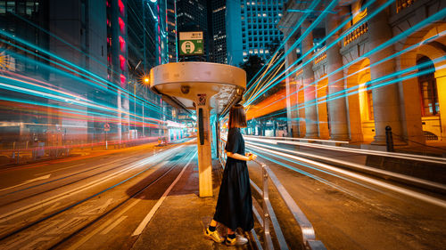 Woman standing amidst light trails on road at night