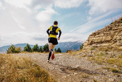 Rear view of man running mountain against sky