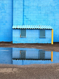 Geometric blue wall and air ducts on back of building reflected in a puddle. 
