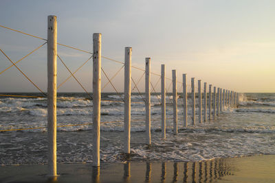 Wooden posts on beach against sky during sunset