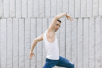 Portrait of young man with arms raised dancing by wall