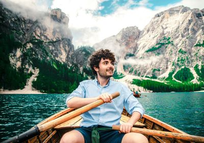 Young man sitting on boat against mountains