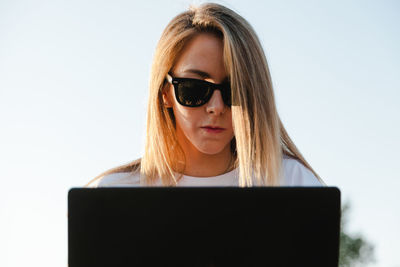 Woman using laptop while sitting against sky