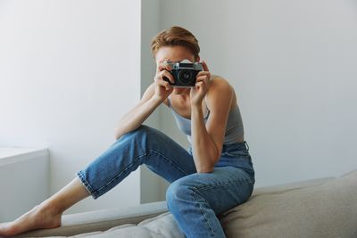 Young woman photographing while sitting on sofa at home