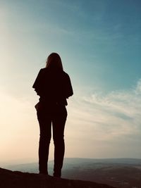 Rear view of silhouette woman standing by sea against sky