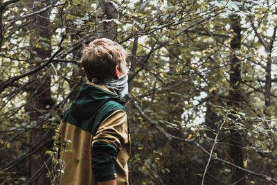 Boy standing against trees in forest