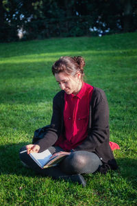 Young woman sitting on book in field