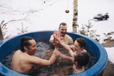 Cheerful mature men and boys giving high-five to each other while taking bath in hot tub