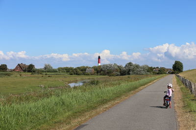 Man riding bicycle on road amidst field against sky