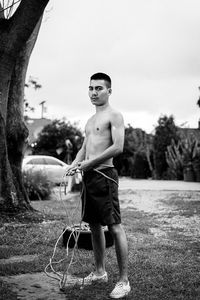 Portrait of shirtless boy standing on grass against sky