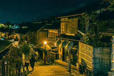 People walking on illuminated street amidst buildings in city at night