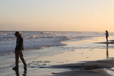 Silhouette man walking on beach against sky during sunset