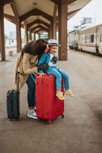 Full length of mother with son wearing mask standing on railroad station platform