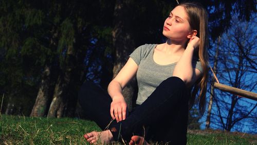 Young woman looking away while sitting on field