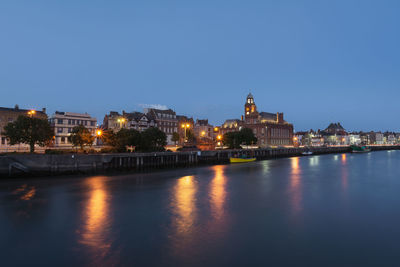 Illuminated buildings by river against clear sky at night