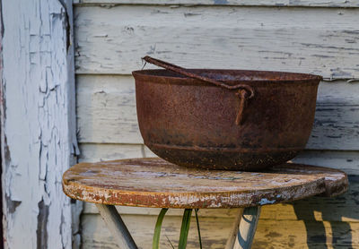 Close-up of rusty metallic bowl on table against wall