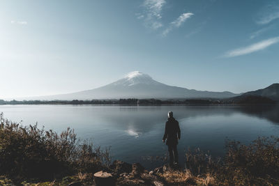 Rear view of man standing by lake against sky