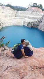 Man kissing woman while sitting on mountain against lake