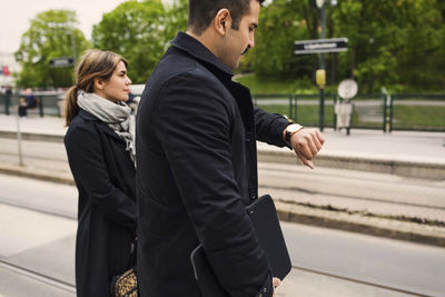 Man checking time while standing by female passenger at tram station