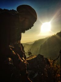 Side view of man on rock against sky during sunset