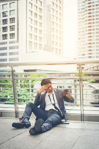 Businessman looking at wallet while sitting on elevated walkway