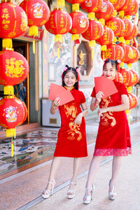 Portrait of smiling girls in red dress against lanterns outdoors